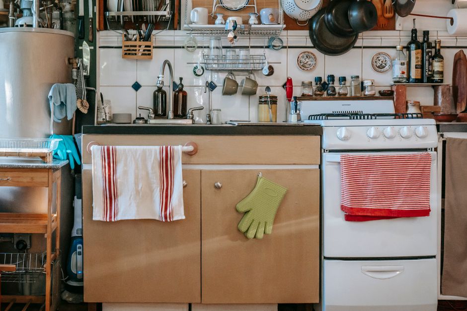 Sink with cabinet under shelves with frying pans and bottles in kitchen with ceramic wall